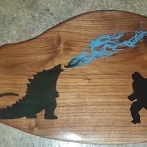 Live edge wood piece with Godzilla and King Kong silhouettes and blue resin flame
